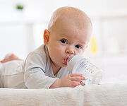 Ein Säugling liegt bäuchlings auf einer Decke und nuckelt an einer Trinkflasche mit Wasser.