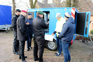 Sechs Personen stehen vor einem blauen Transportfahrzeug, vier der Personen tragen Uniform von Bundeswehr, Katastrophenschutz und Feuerwehr