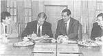 Ausgeglichenes schwarz-weiß Foto: Vier Herren in Anzügen an einem Tisch während einer Vertragsunterzeichnung