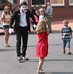 Schnappschuss der Einweihungsfeier: ein Pantomimen-Clown mit weiß geschminkten Gesicht, schwarzem Anzug und weißen Handschuhen in einer Gruppe von Kindern