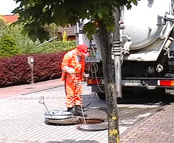 Ein Kanalarbeiter steht auf der Straße vor einem geöffneten Gullydeckel und hantiert am Schacht..