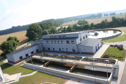 Luftbild dreier rechteckiger Becken vor dem Betriebsgebäude; im Hintergrund das kreisrunde Belebungbecken.
