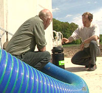 Zwei Landwirte knien vor einem nicht näher erkennbaren technischen Gerät.
