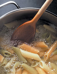 Kochende Nudeln in einem Kochtopf werden mit einem Holzlöffel umgerührt.