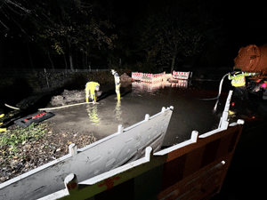 Nachtaufnahme einer überfluteten Straße; Arbeiter mit einem Tankwagen versuchen, Wasser abzupumpen.