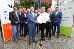 Eine Gruppe von elf Personen steht zwischen zwei Werbebannern der Klärschlammverwertung und der Müllverbrennungsanlage und präsentieren ein Dossier.