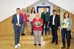 Die in den Ruhestand gehende Mitarbeiterin mit einem Blumenstrauß ist umringt von sechs Kolleg*innen.