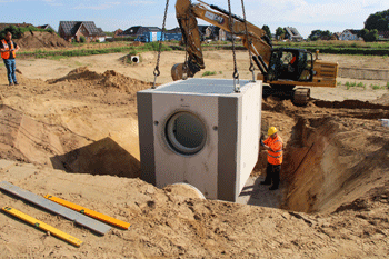 Ein Raupenbagger hebt den Betonblock des Drosselbauwerks in den bereits ausgeschachteten Kanal.
