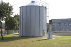 Ein 12 m hoher zylinderförmiger Turm mit chronisch zu laufendem Deckel davor ein etwa halb so hohes, säulenartiges Bauteil zum Abfackeln des Gases.