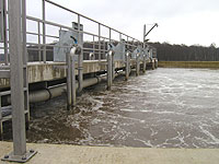 Blick über die Wasseroberfläche des kreisrunden Belebungbeckens sowie auf die Brücke mit den Rührwerken.