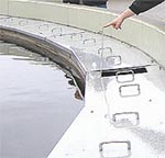 Ausschnitt des Begrenzungsrandes des Nachklärbeckens. Eine Hand zeigt auf ein Detail.