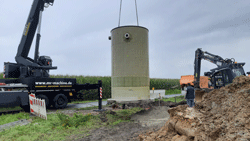 Ein Kranwagen hebt das zylinderförmige Zwischenpumpwerk in den Kanalschacht.
