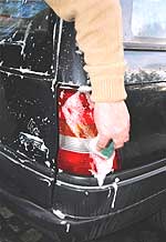 Eine Hand wäscht das Rücklicht eines PKW mit schaumigem Wasser.