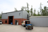 Das zweigeschossige Betriebsgebäude und das Becken der Floatation Anlage, davor ein Transporter mit Anhänger.