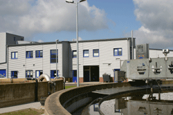 Flacher Blick über deinen Teil des kreisrunden Nachklärbeckens auf das Betriebsgebäude