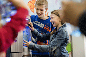 Zwei Kinder stehen lachend an einem Trinkwasserspender.