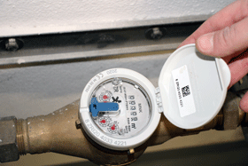 Eine Hand öffnet den Deckel, hinter dem sich die Anzeige eines Wasserzählers befindet.