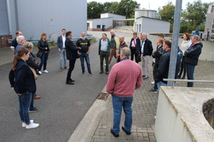 Eine Gruppe von etwa 20 Menschen diskutiert auf dem Betriebsgelände einer Kläranlage.