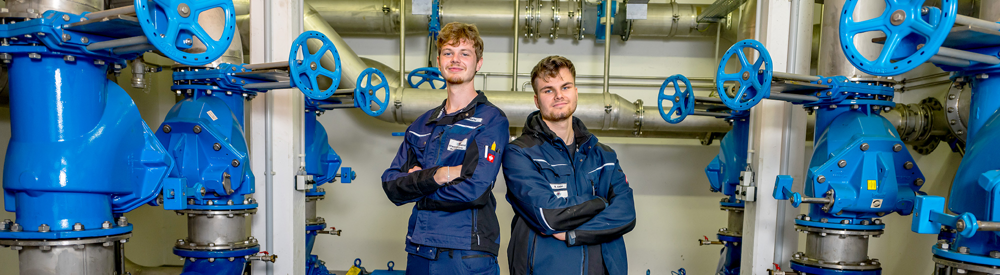 Zwei junge Männer in einem Pumpenraum auf der Kläranlage. Zwei junge Männer in einem Technikraum.