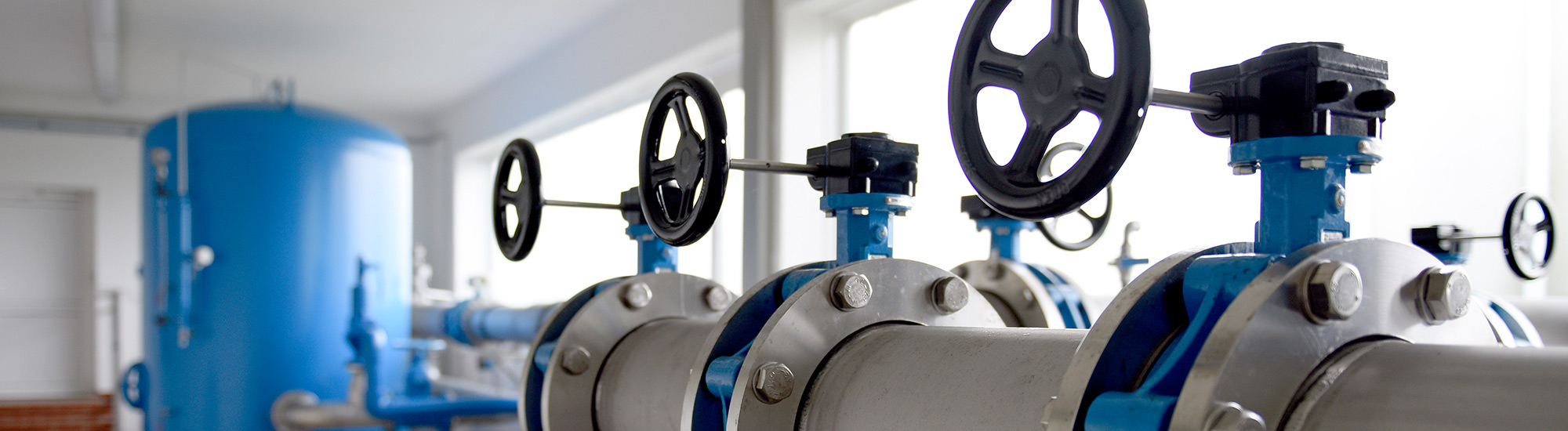 Drei Absperrventile mit kreisrunden Drehrädern in der Betriebshalle eines Wasserwerkes.