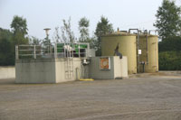 Zwei zylinderförmige Türme neben einem quaderförmigen Betonblock, der von einem Geländer umgeben ist.