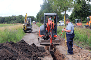 zwei kleine Bagger und Menschen auf einer Baustelle. Eine Schmutzwasserleitung wird verlegt.