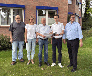 Fünf menschen. Vier Männer und eine Frau überreichen eine Urkunde.