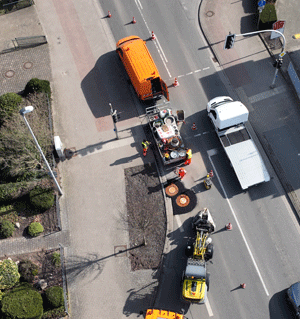 Luftbild von Straße mit Fahrzeugen und reparierten Kanaldeckeln.