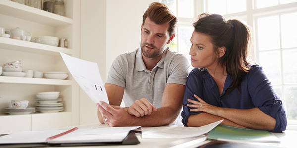 Ein junges Paar sitzt an einem Küchentisch, auf dem diverse Papiere ausgebreitet sind. Sie schauen gemeinsam auf eines der Blätter.
