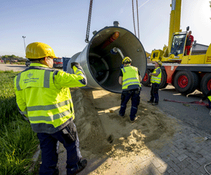 Drei Bauarbeiter mit großem Pumpenschacht auf einer Baustelle.