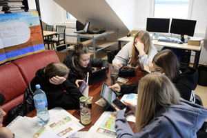 Eine Gruppe Schüler*innen sitzt an einem Tisch um einen Laptop herum.