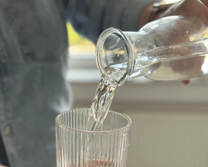 Aus einer Glasflasche wird Trinkwasser in ein Glas gefüllt.