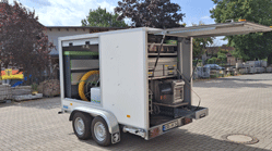 Ein Autoanhänger, der geöffnet ist und das Innleben zeigt. Zu sehen sind ein Wassertank sowie die technische Ausstattung.