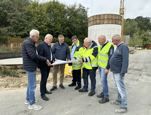Gruppe von sieben Männern mit Bauplan auf einer Baustelle vor neuem Behälter.