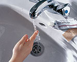 Eine Hand mit ausgestrecktem Finger unter dem Wasserstrahl einer Waschbecken-Armatur.