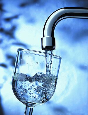 Aus einem Wasserhahn läuft Wasser sprudelnd in ein Glas