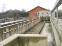 Ein langgestreckter Schacht, abgegrenzt durch eine Mauer und weitere technische Einrichtungen, führt auf das Betriebsgebäude zu.